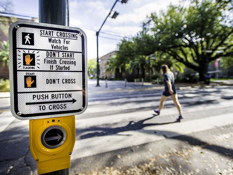 Instructions for button that triggers crosswalk lights with blurred student crossing street in background.