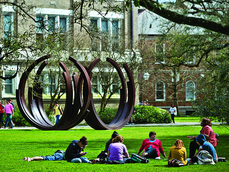 Students sitting in the grass near a round sculpture.